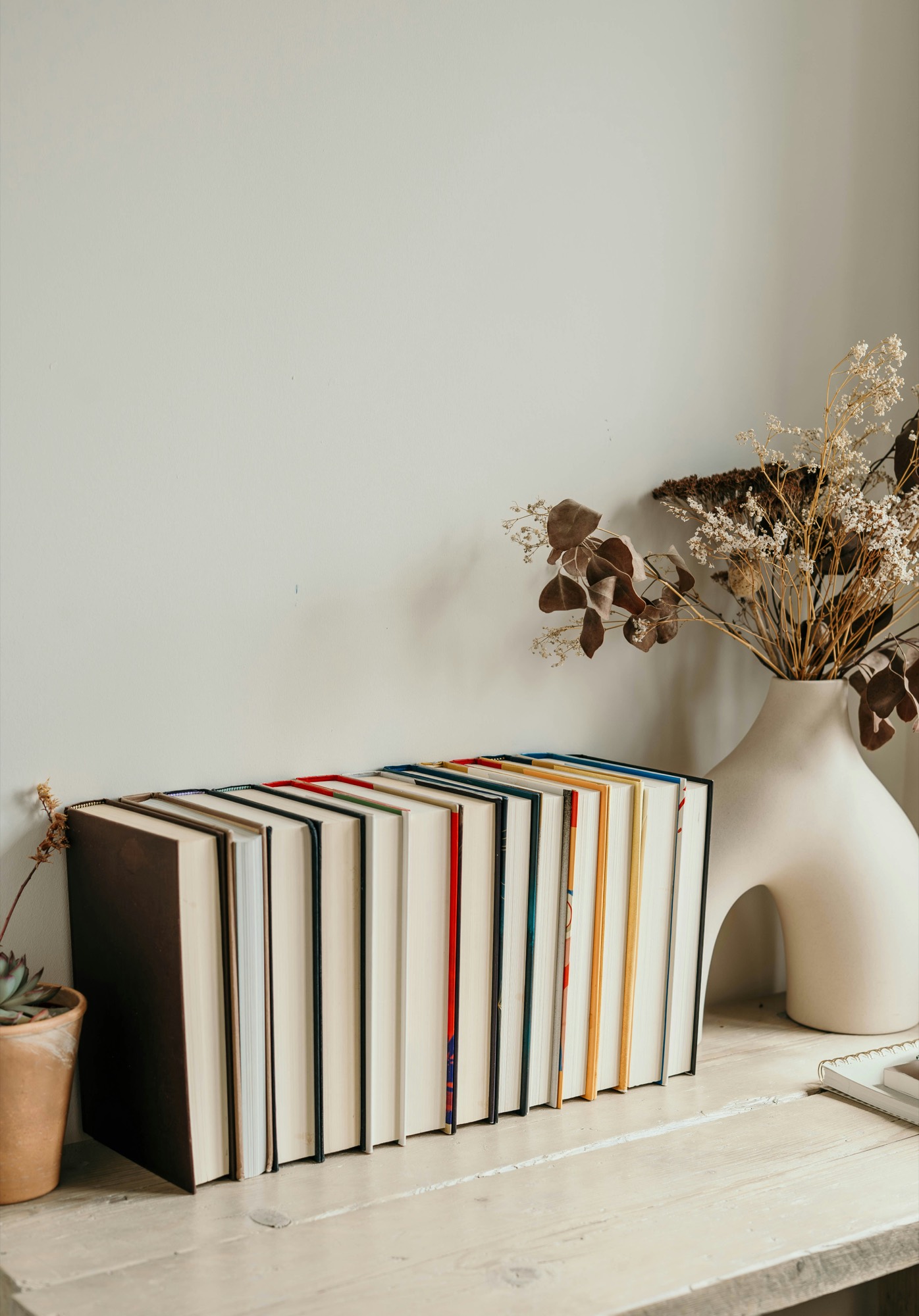 A shelf of hardcover books beside a vase