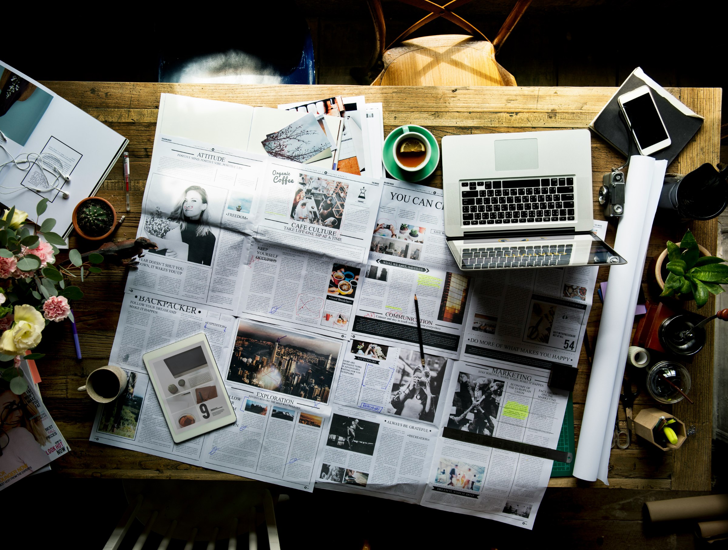 Newspaper spreads, a laptop, and a tablet on a work desk